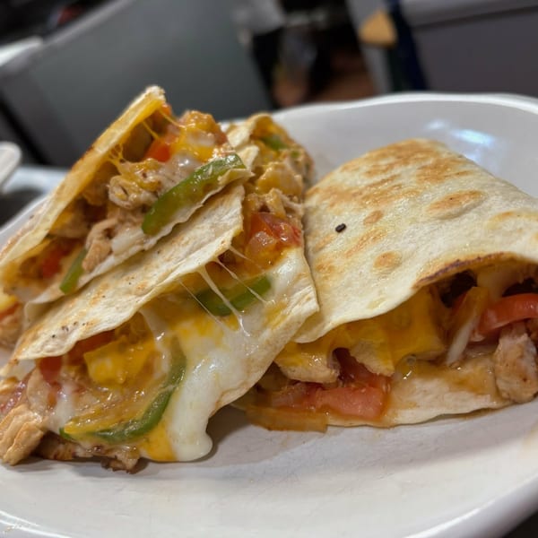 Two cheesy chicken quesadillas with melted cheese, green peppers, and tomatoes on a white plate.