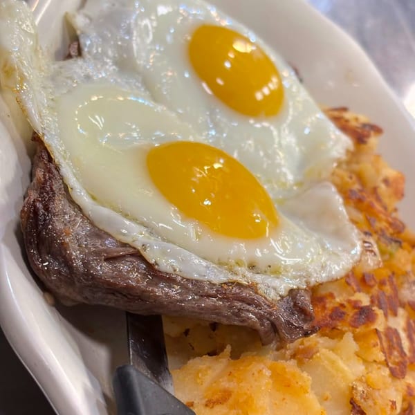 Close-up of steak and hash browns topped with two sunny-side-up eggs on a white plate.