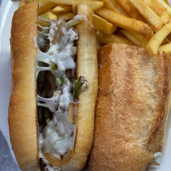 A close-up of a cheesy steak and pepper sub with a side of golden french fries.