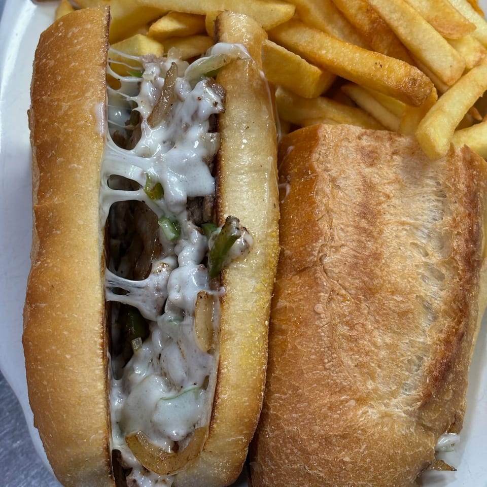 A close-up of a cheesy steak and pepper sub with a side of golden french fries.