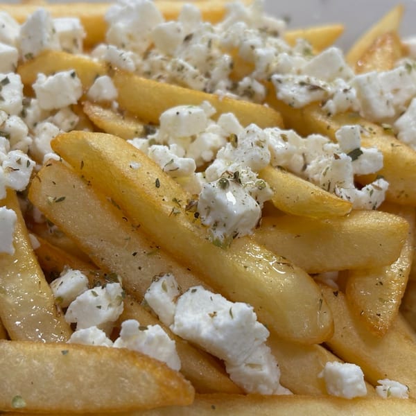 Close-up of golden french fries topped with crumbled feta cheese and dried herbs.