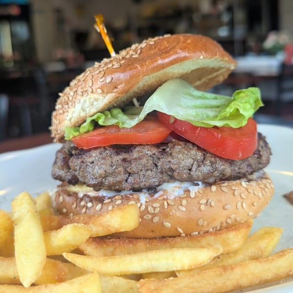 A juicy burger with lettuce, tomato, and sauce on a sesame bun, served with golden fries.