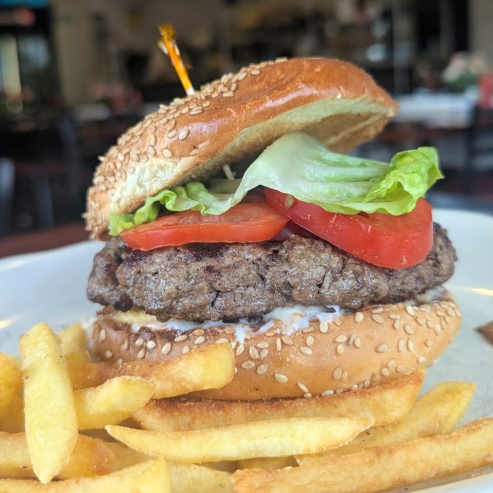 A juicy burger with lettuce, tomato, and sauce on a sesame bun, served with golden fries.
